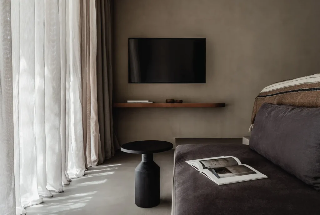 Develine Microcement warm taupe wall and gray floor in a luxury bedroom suite with wall-mounted TV and velvet daybed
